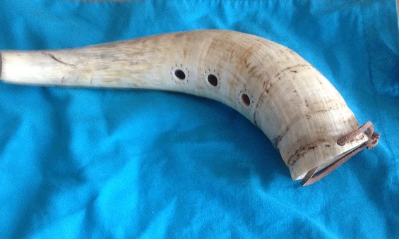 A beige horn with three finger holes and a leather strap at the mouth. The horn lies on a blue cloth.