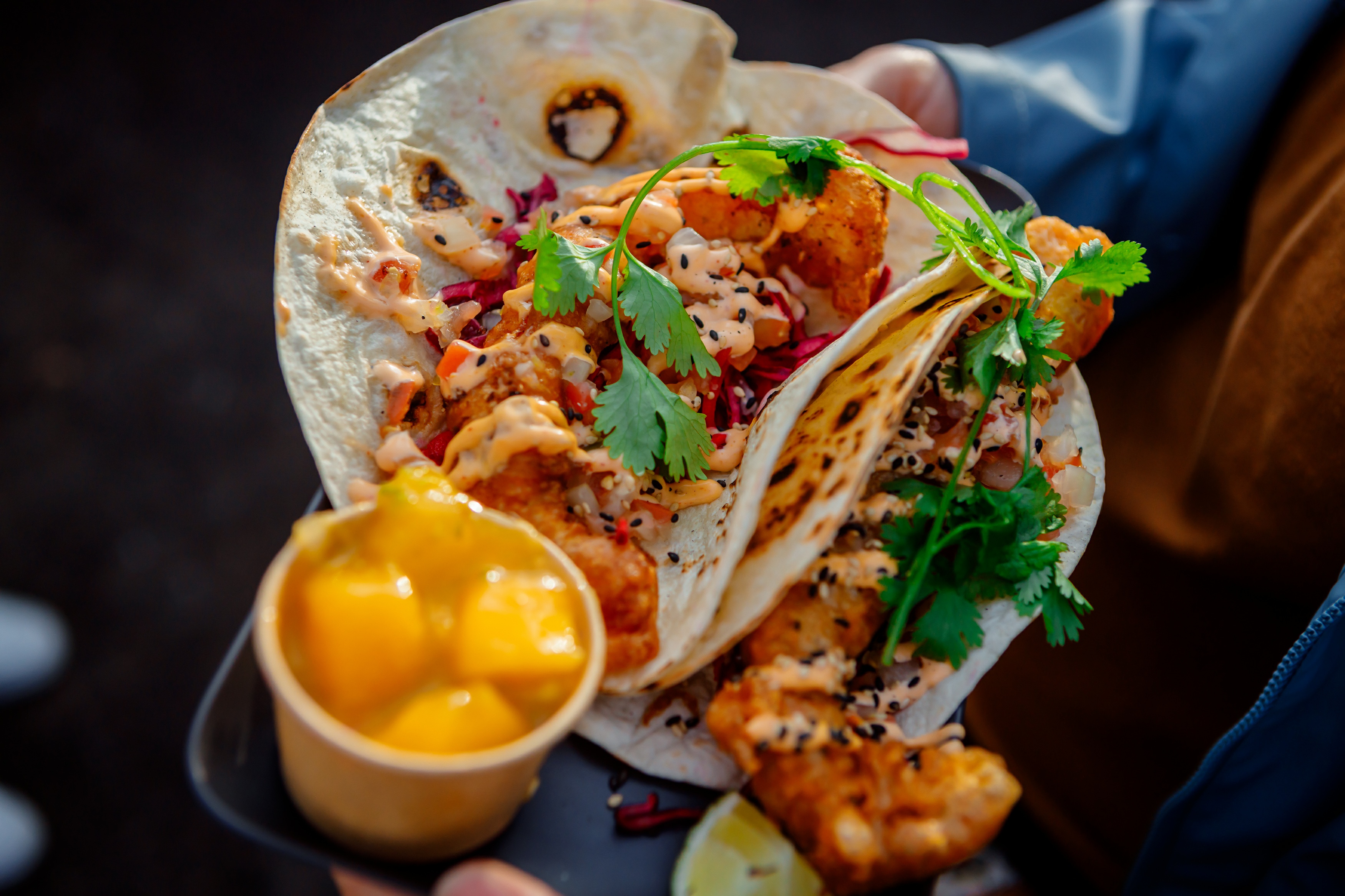 Tacos med en orange sås, friterat innehåll och en skål med mango.