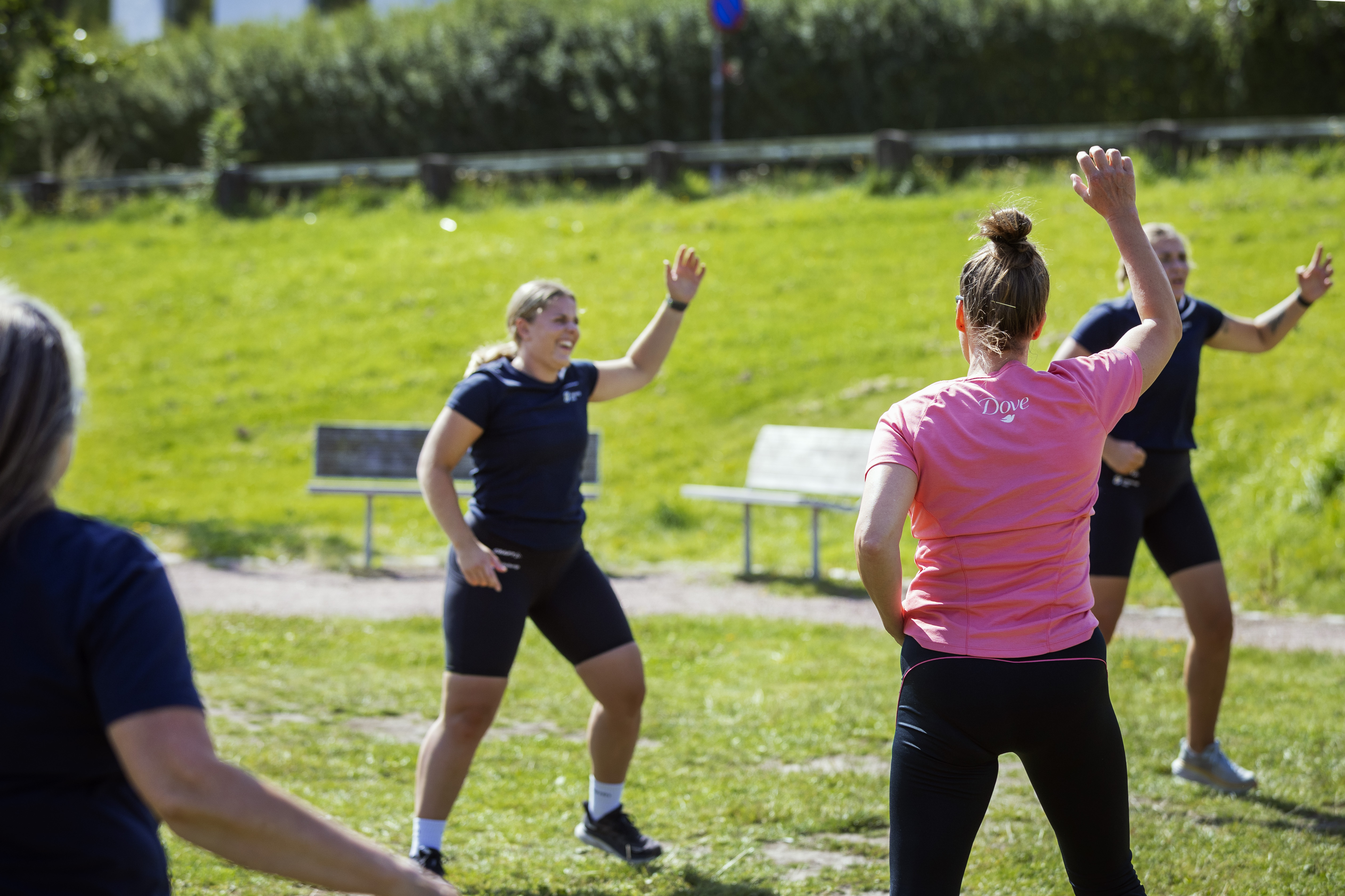 En person som har på sig sportkläder står mitt i en rörelse på en grön gräsmatta. Framför står flera personer och härmar rörelserna.