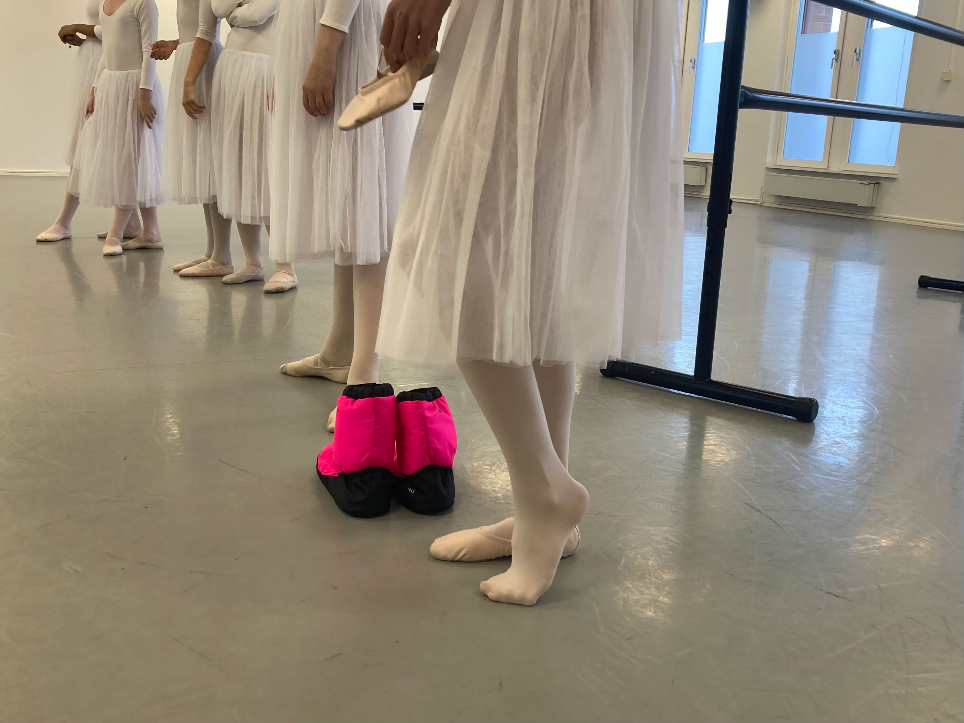 Flera balettdansöser står på rad i en danssal. Alla har på sig vita kjolar och balettskor.