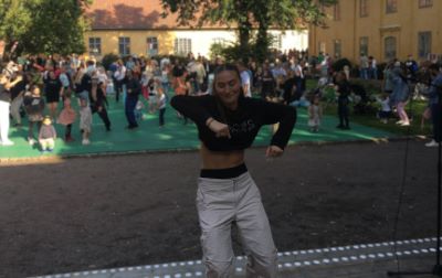 En tjej i mörk tröja och ljus byxor dansar med flera dansande personer i bakgrunden.
