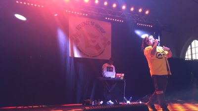 Person som står på scenen och sjunger, bakom hen står en DJ vid ett mixerbord.