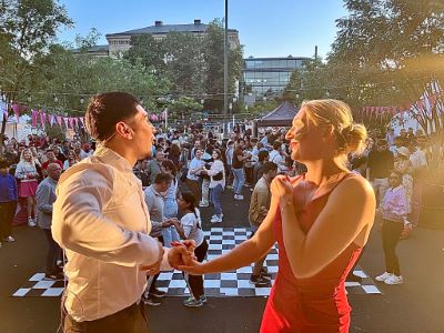 Svenska: Ett par dansar på ett rutigt dansgolv utomhus, omgivna av en stor publik i kvällsljus.