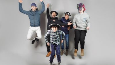 Fem personer hoppar upp i luften och gör glada gester. Tre av personerna har på sig hattar.
