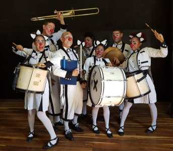 Sju män med clownkostymer och musikinstrument poserar roligt.