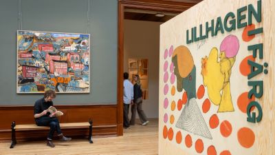 Ett utställningsrum på ett museum med tavlor på väggarna. I förgrunden syns en färgglad tavla med texten