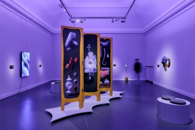 Ett museumrum i lila belysning med modern konst på väggarna och ett stort tredelat skärmverk i mitten med surrealistiska objekt.