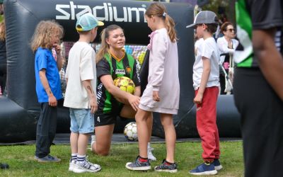 Fyra barn står runt om en fotbollsspelare som sitter på knä och håller i en fotboll.