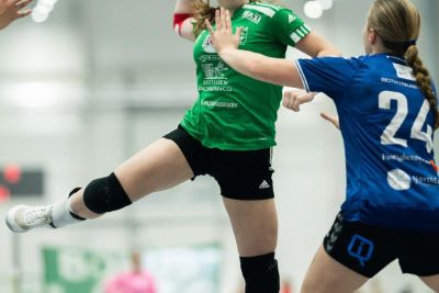 En handbollspelare som hoppar upp i luften med en grön tröja.